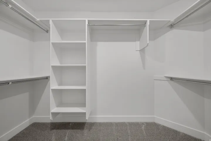 Built-in Master closet system featuring white shelving, multiple hanging rods, and grey carpet flooring