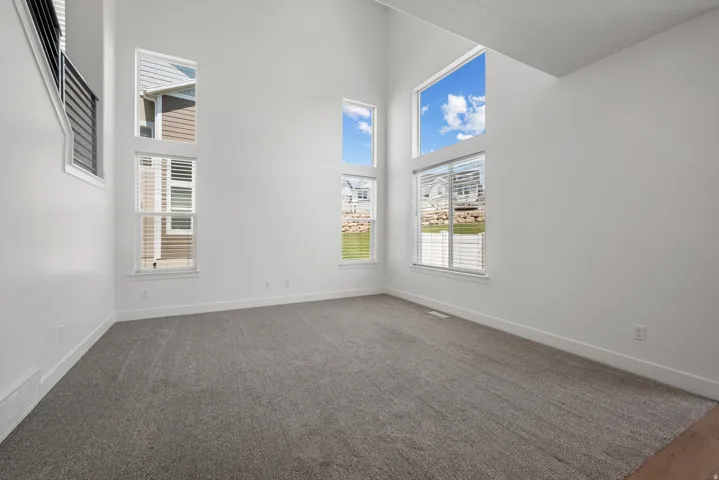 Two-story room featuring a soaring ceiling, multiple large windows, horizontal blinds, and neutral grey carpeting