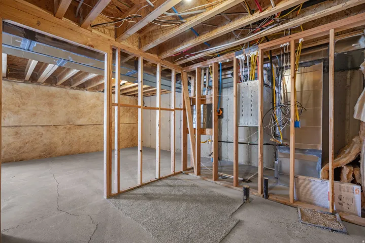 Unfinished basement featuring exposed wood framing, concrete flooring, and visible electrical conduit