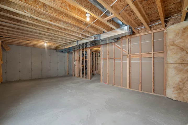 Unfinished basement featuring concrete flooring, exposed wood joists, structural framing, and visible insulation