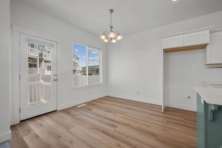 Bright and spacious room featuring warm wood-finish flooring, abundant natural light from dual windows, and a contemporary pendant light fixture