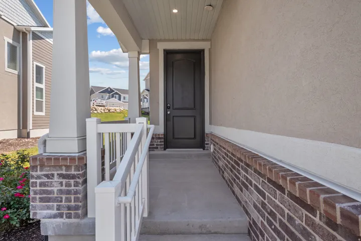 Inviting entryway featuring a dark paneled door, concrete porch, white column supports, and a brick facade
