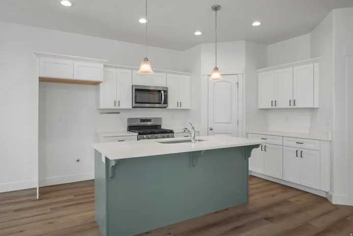 Kitchen featuring a central island with a contrasting base, white shaker-style cabinetry, stainless steel appliances, recessed lighting, and wood-finish flooring
