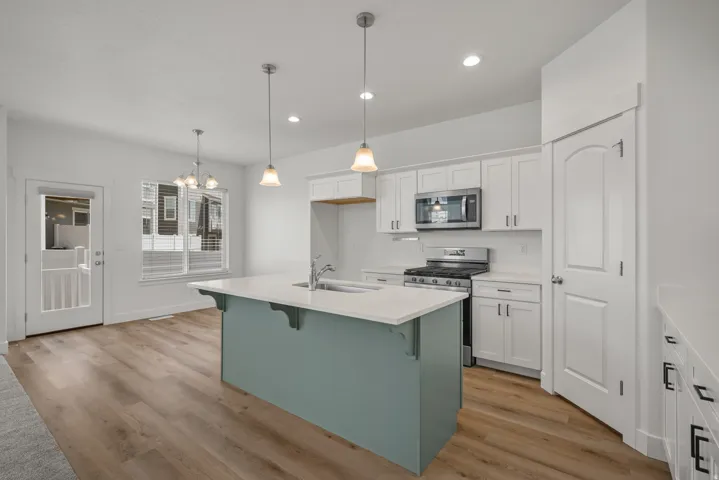Modern kitchen featuring a light blue island with counter seating, white cabinetry, stainless steel appliances, and light-tone wood-finish flooring