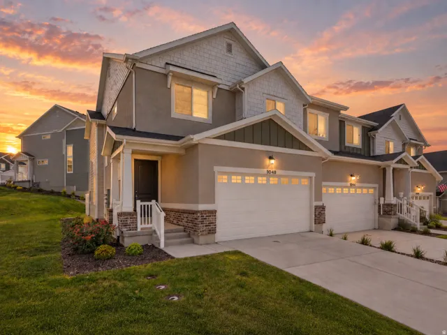 Contemporary exterior featuring a covered entry, two-car garage, brick accents, and a landscaped front yard