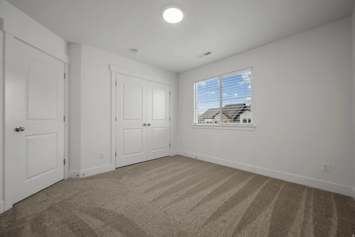 Carpeted room featuring a double-pane window with blinds, white trim, a flush-mount ceiling light, and two white paneled doors