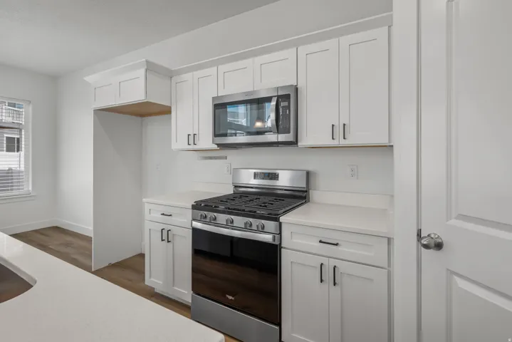 Modern kitchen featuring white shaker cabinetry, stainless steel appliances, white countertops, and wood-finish flooring