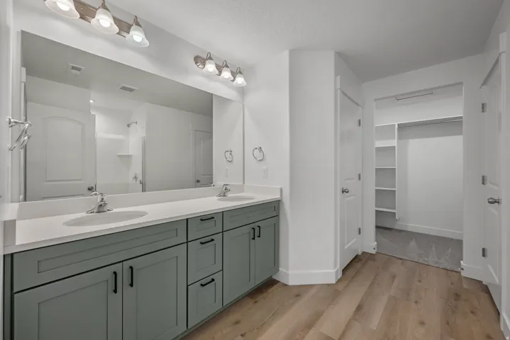 Bathroom featuring a dual vanity with a light gray countertop and matte black hardware, dual overhead vanity lighting, a large mirror, and wood-finish flooring