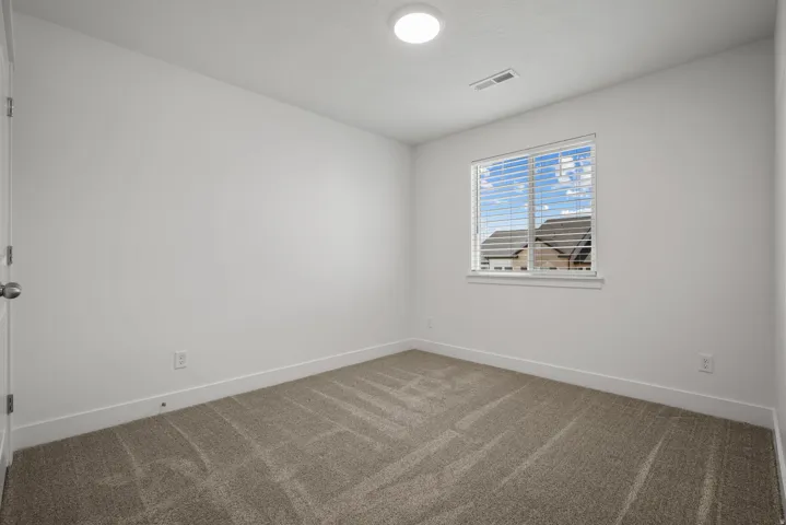 Carpeted room featuring a single window with blinds, a white door, overhead flush-mount lighting, and white baseboards