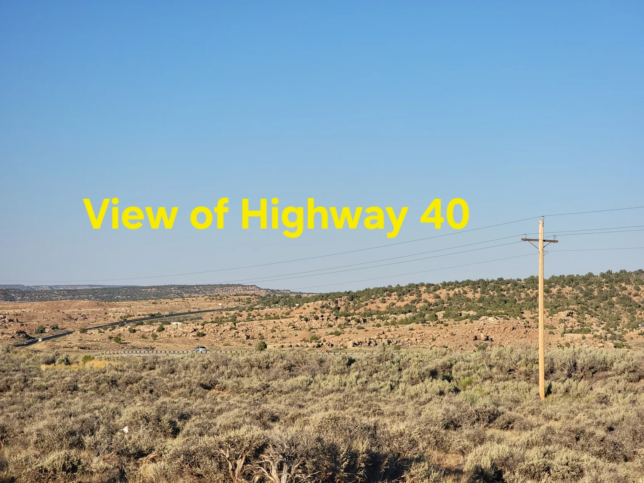 Expansive desert landscape featuring natural brush, distant highway, and clear sky