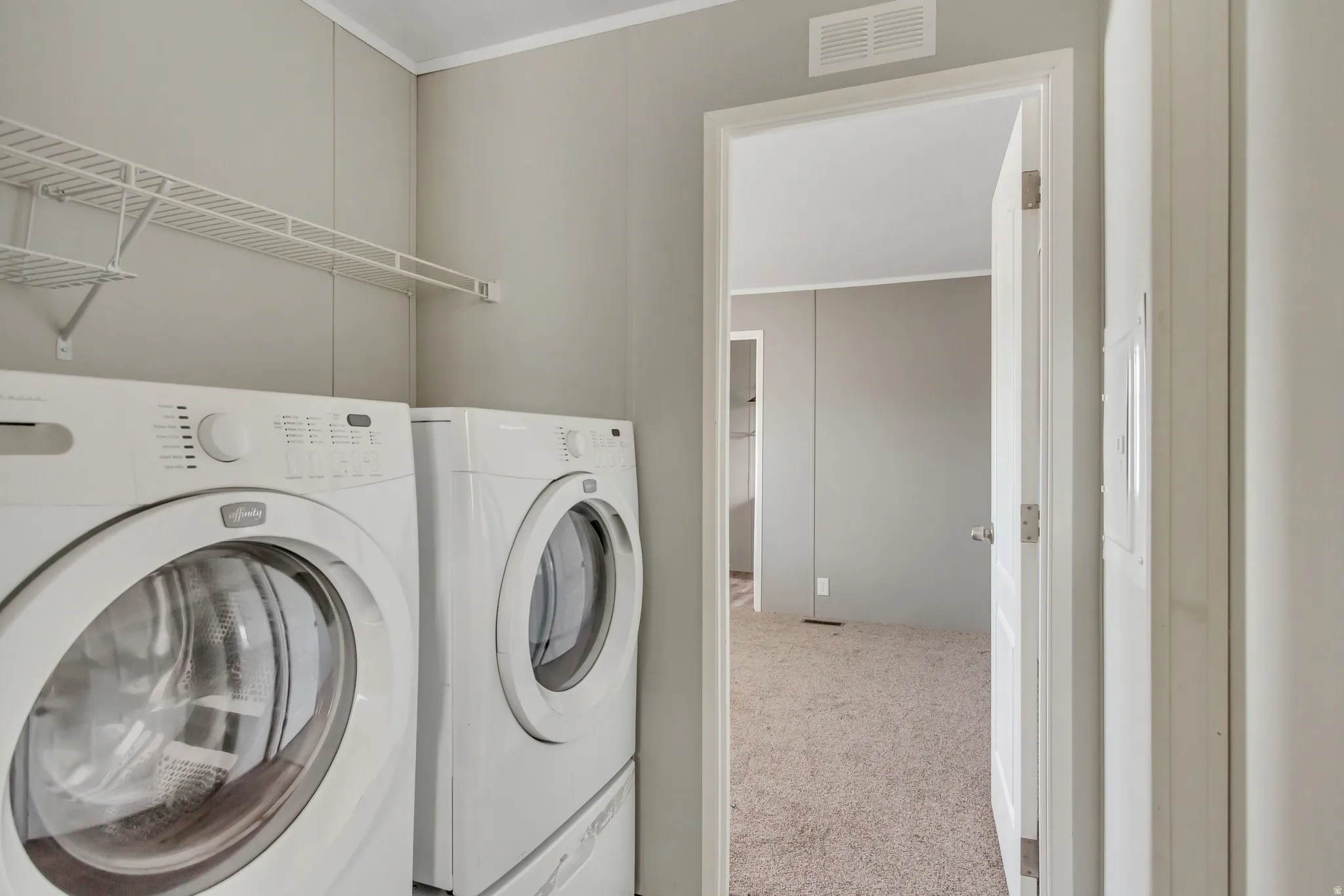 Laundry area with light gray paneled walls, white wire shelving, and overhead ventilation