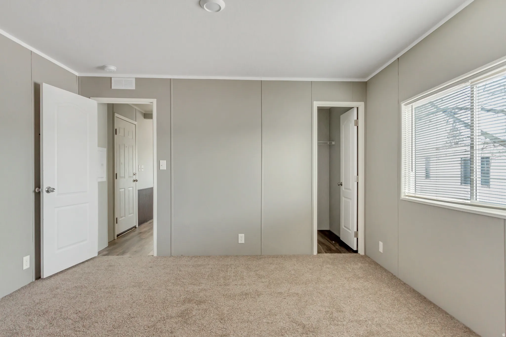 Carpeted room with a large window featuring horizontal blinds