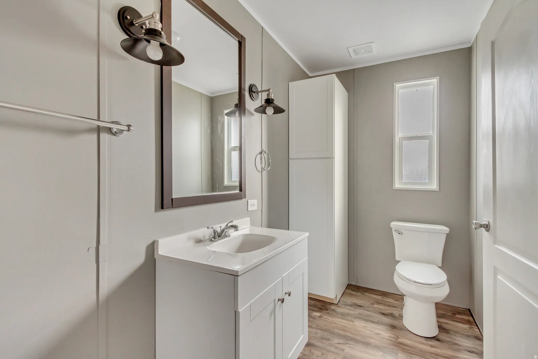 Bathroom featuring a white vanity with integrated sink, a rectangular mirror, and wall-mounted light fixtures