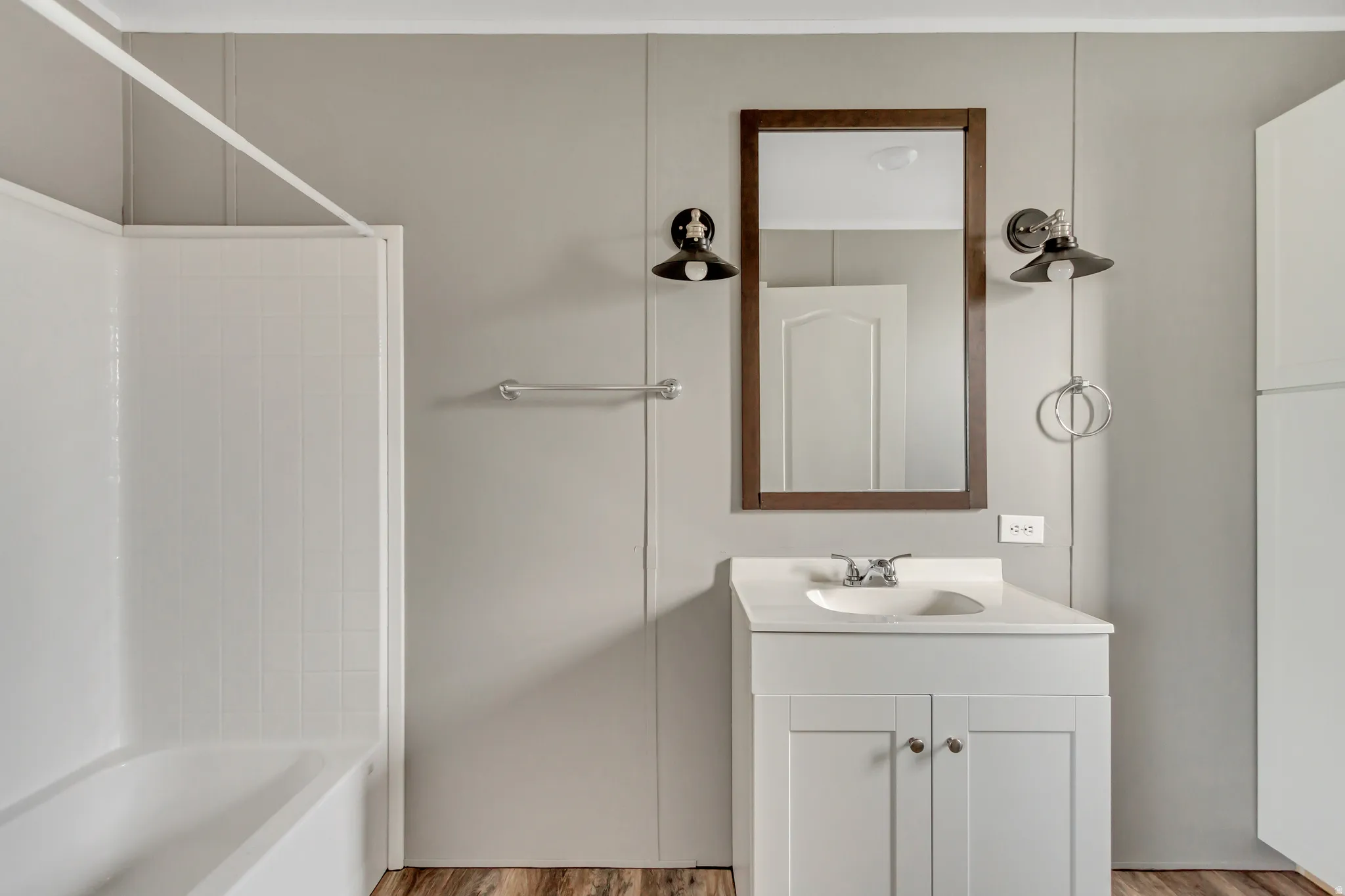 Bathroom featuring a white vanity with integrated sink, chrome faucet, and wood-finish flooring