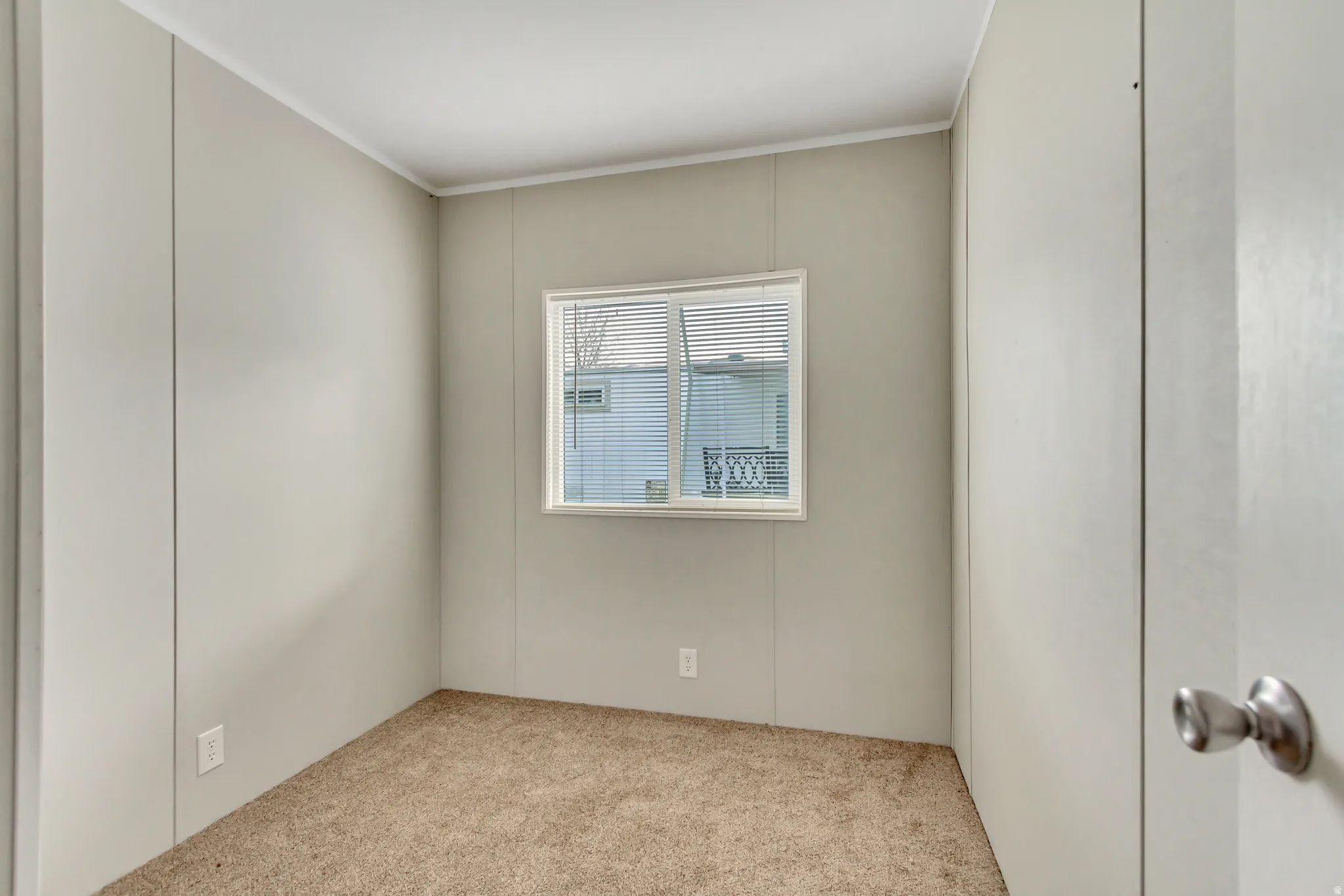 Bright bedroom featuring neutral carpeting, clean white walls, and a casement window with blinds allowing natural light