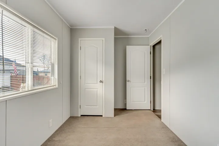 Interior room featuring light gray walls, plush carpeting, and a large window with horizontal blinds