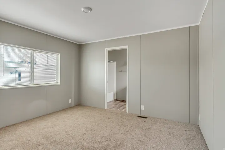 Carpeted room with light grey paneled walls, white trim, and a rectangular window with blinds