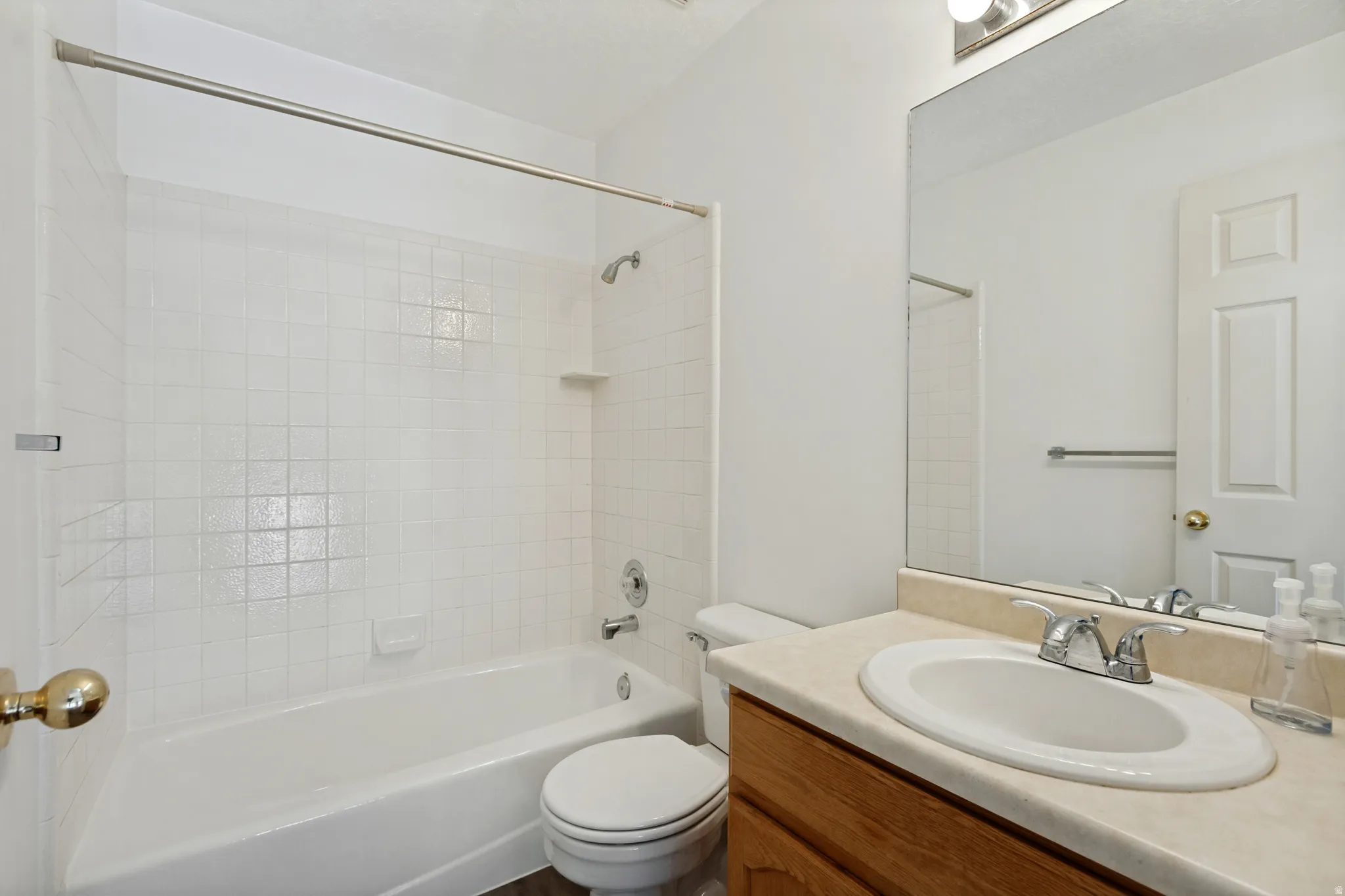 Bathroom featuring a white subway tile tub surround, white bathtub, chrome fixtures, light-toned countertop, and wood-finish vanity