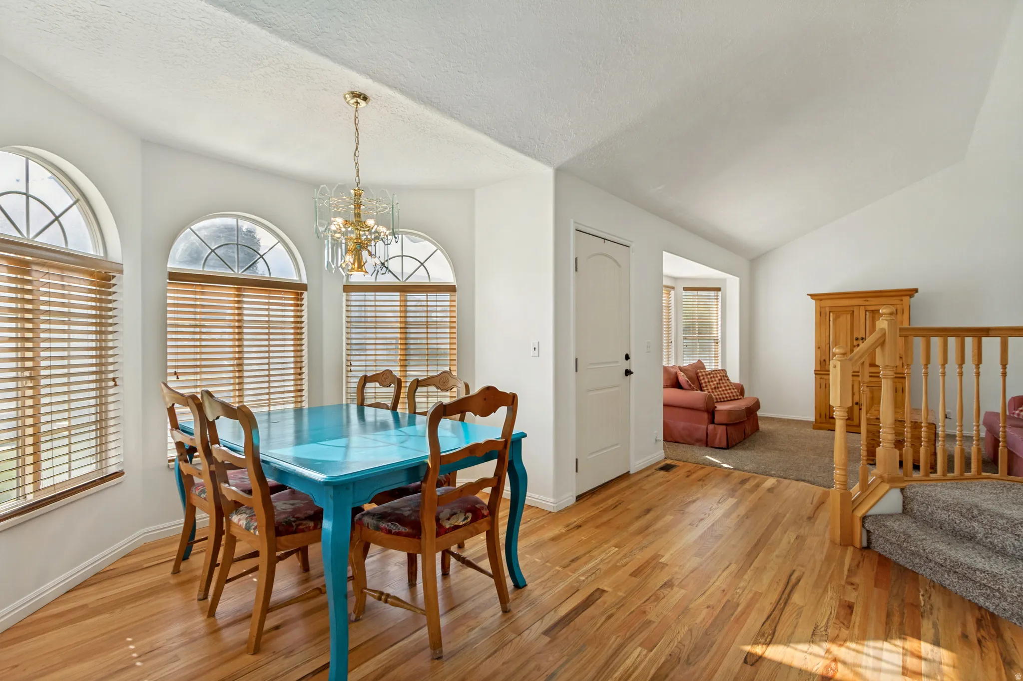 Dining area featuring wood-finish flooring, three arched windows with wood blinds, and a decorative chandelier