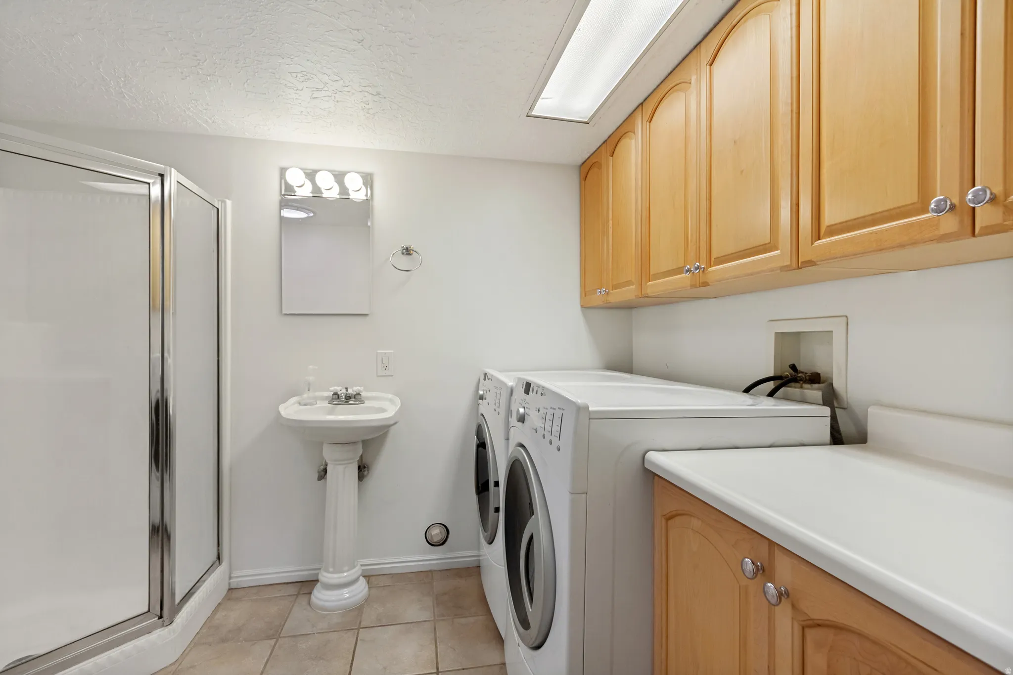 Combined laundry and bath space featuring a standing shower with a glass enclosure, a pedestal sink, and tiled flooring