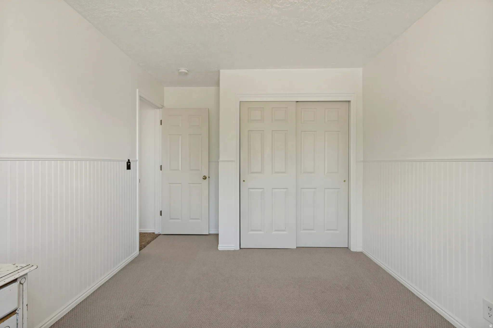 Spacious bedroom featuring neutral carpet flooring, white six-panel closet doors with sliding hardware, wainscoting accent wall paneling, and generous ceiling height with recessed lighting