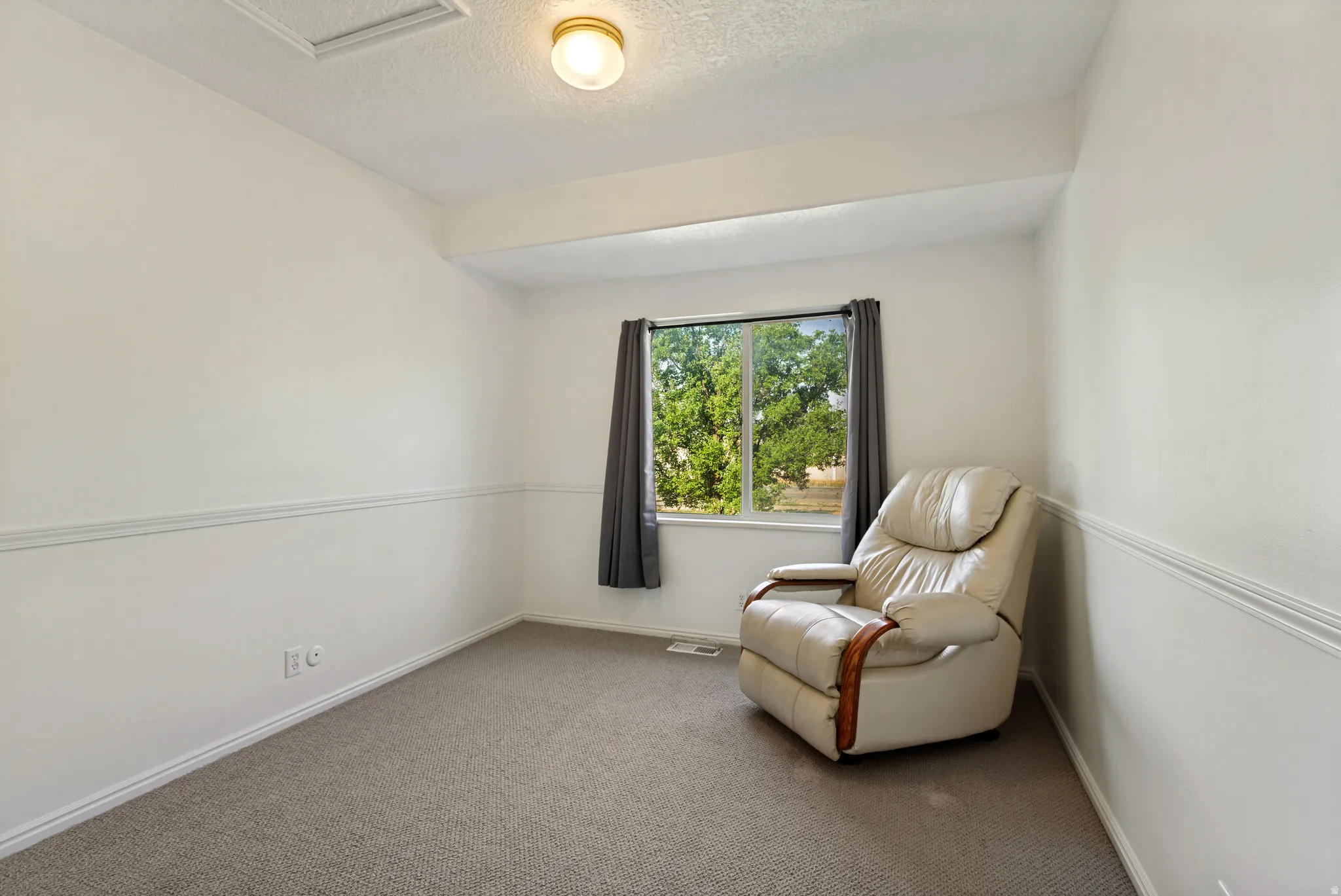 Bright secondary bedroom with neutral wall treatment featuring chair rail molding, carpet flooring, and a large window with natural light and outdoor scenery