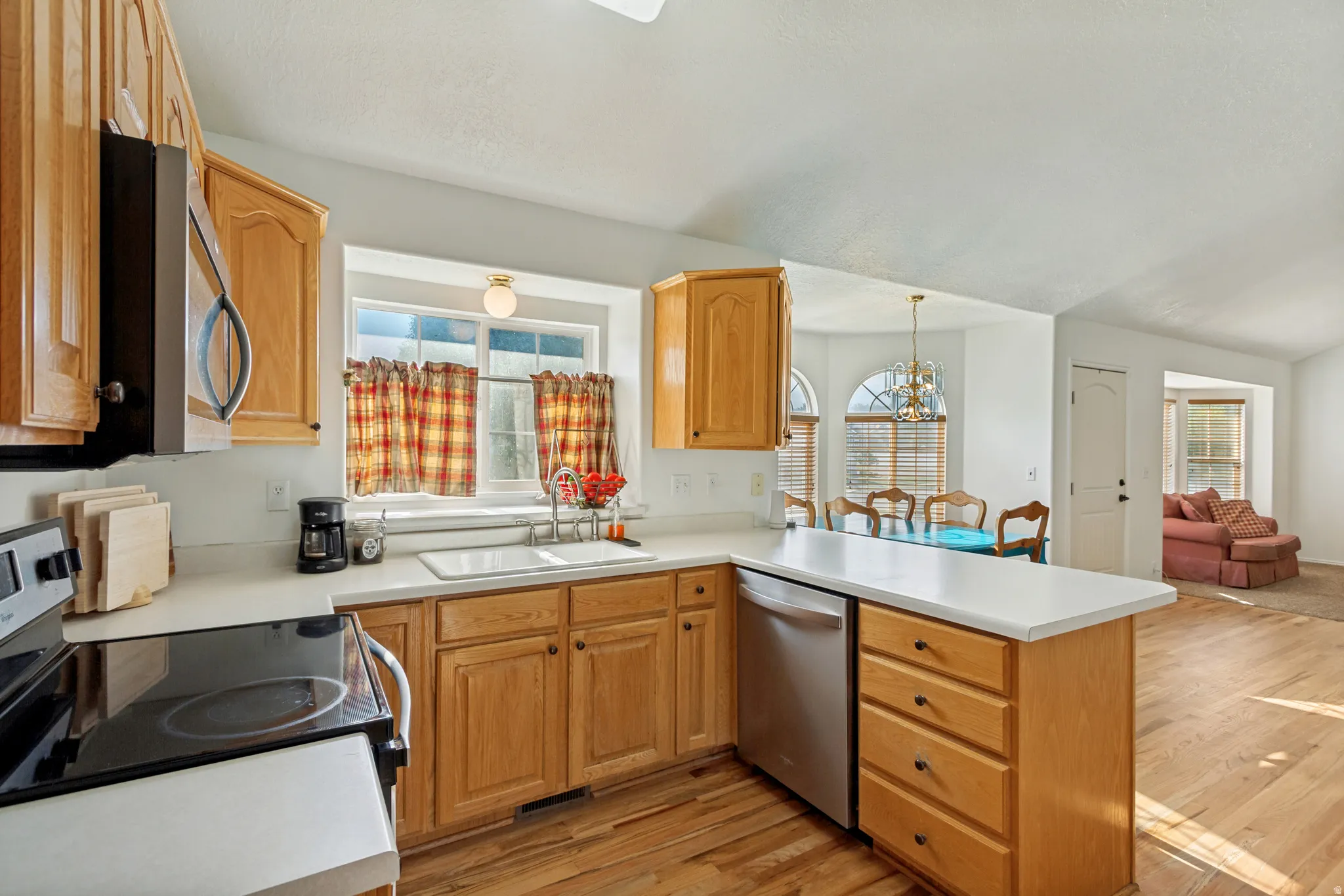 Spacious kitchen featuring warm wood cabinetry, white quartz countertops, a large center island with storage drawers, stainless steel appliances, and abundant natural light from multi-pane windows