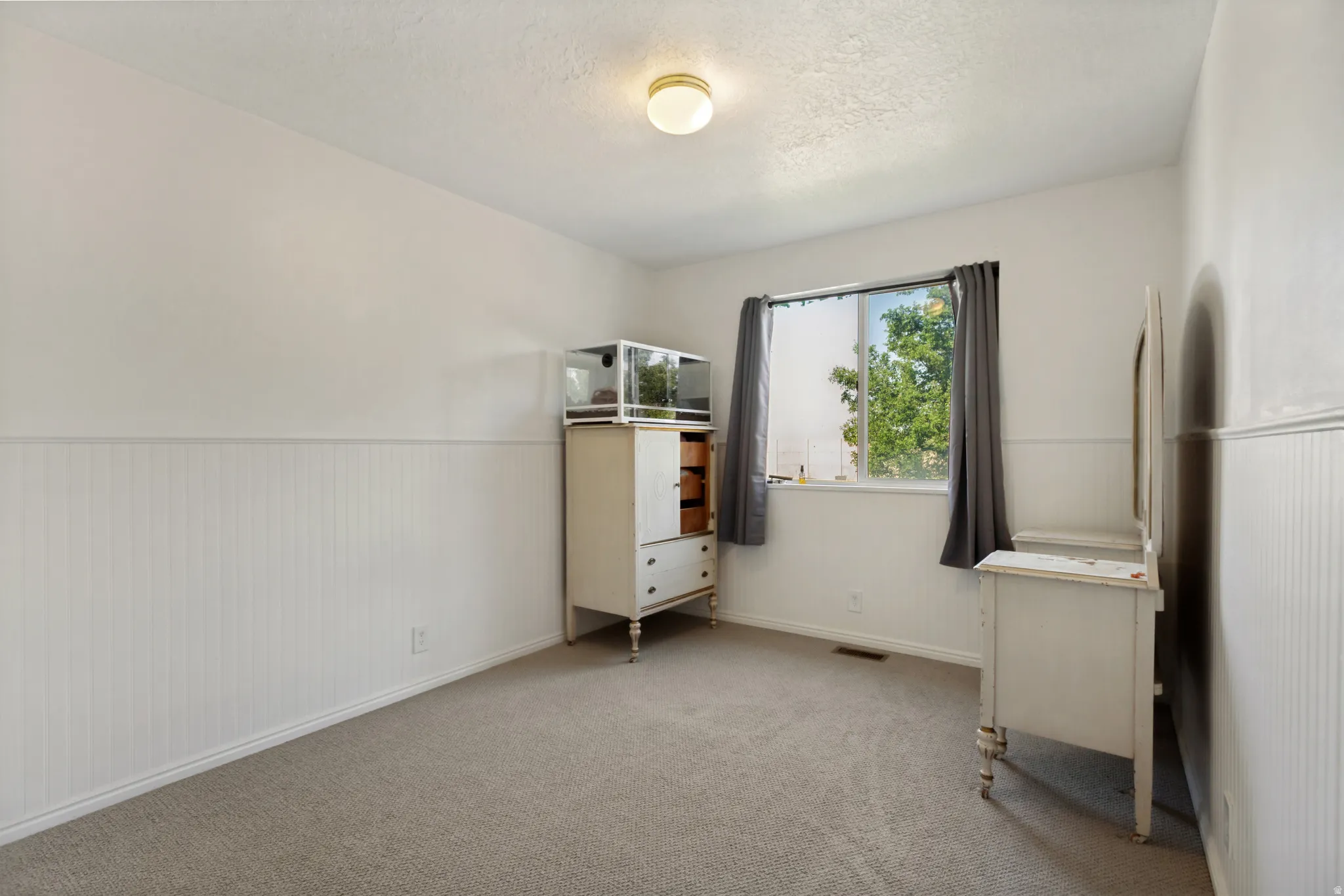 Bright secondary bedroom featuring neutral carpeting, white wainscoting accents, and a large window with natural light