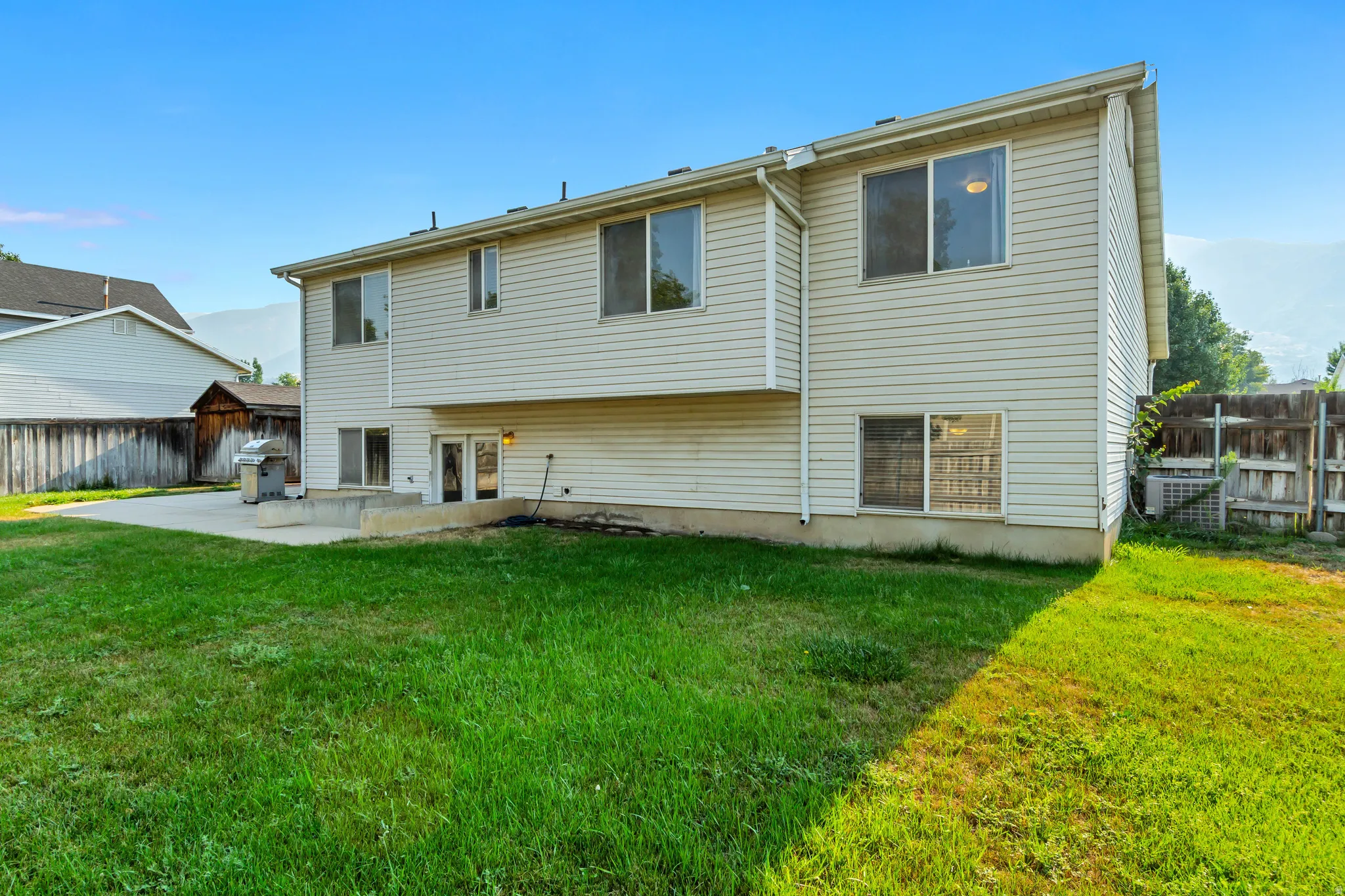 Expansive rear yard featuring a concrete patio, wood fencing, and a two-story exterior with multiple windows