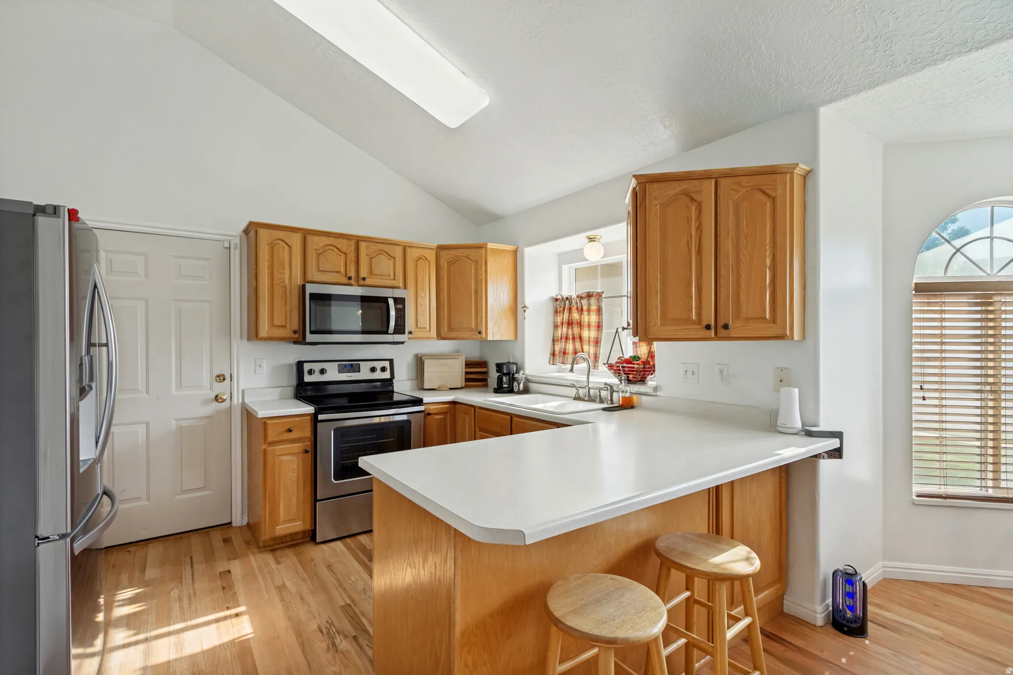 Kitchen featuring wood-finish flooring, light wood cabinetry, white countertops, and stainless steel appliances