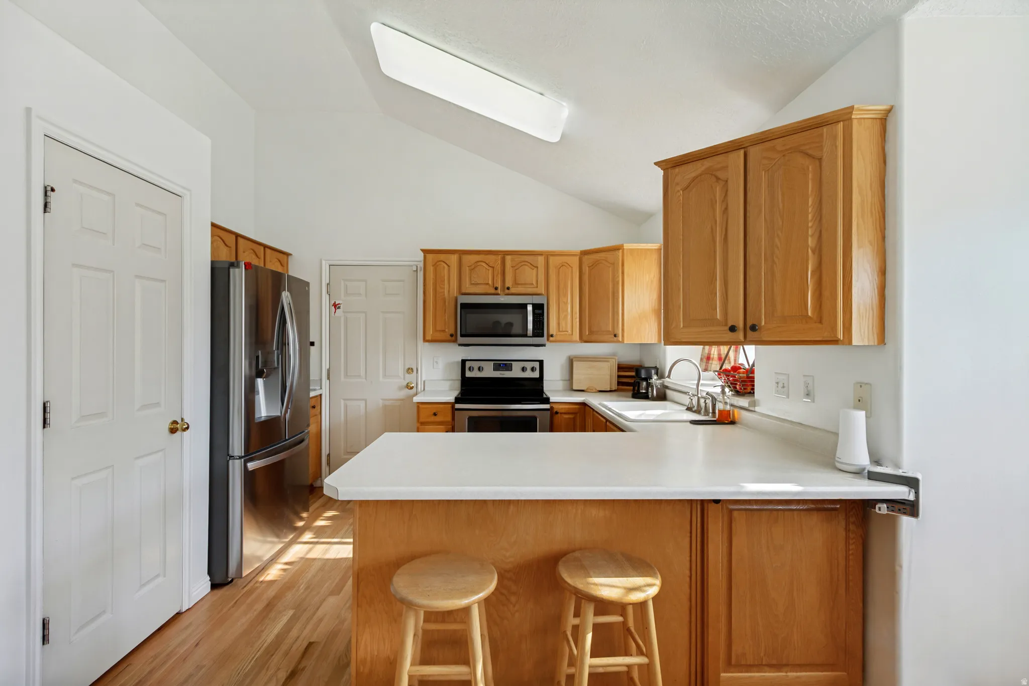 Bright, open kitchen featuring warm wood cabinetry, stainless steel appliances, and a spacious white quartz island with seating for two