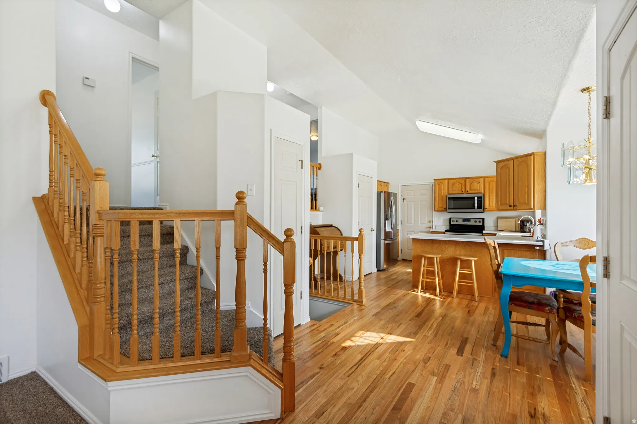 Open-concept living space featuring warm wood-finish flooring throughout, custom wooden staircase with metal balusters, and abundant natural light from skylights