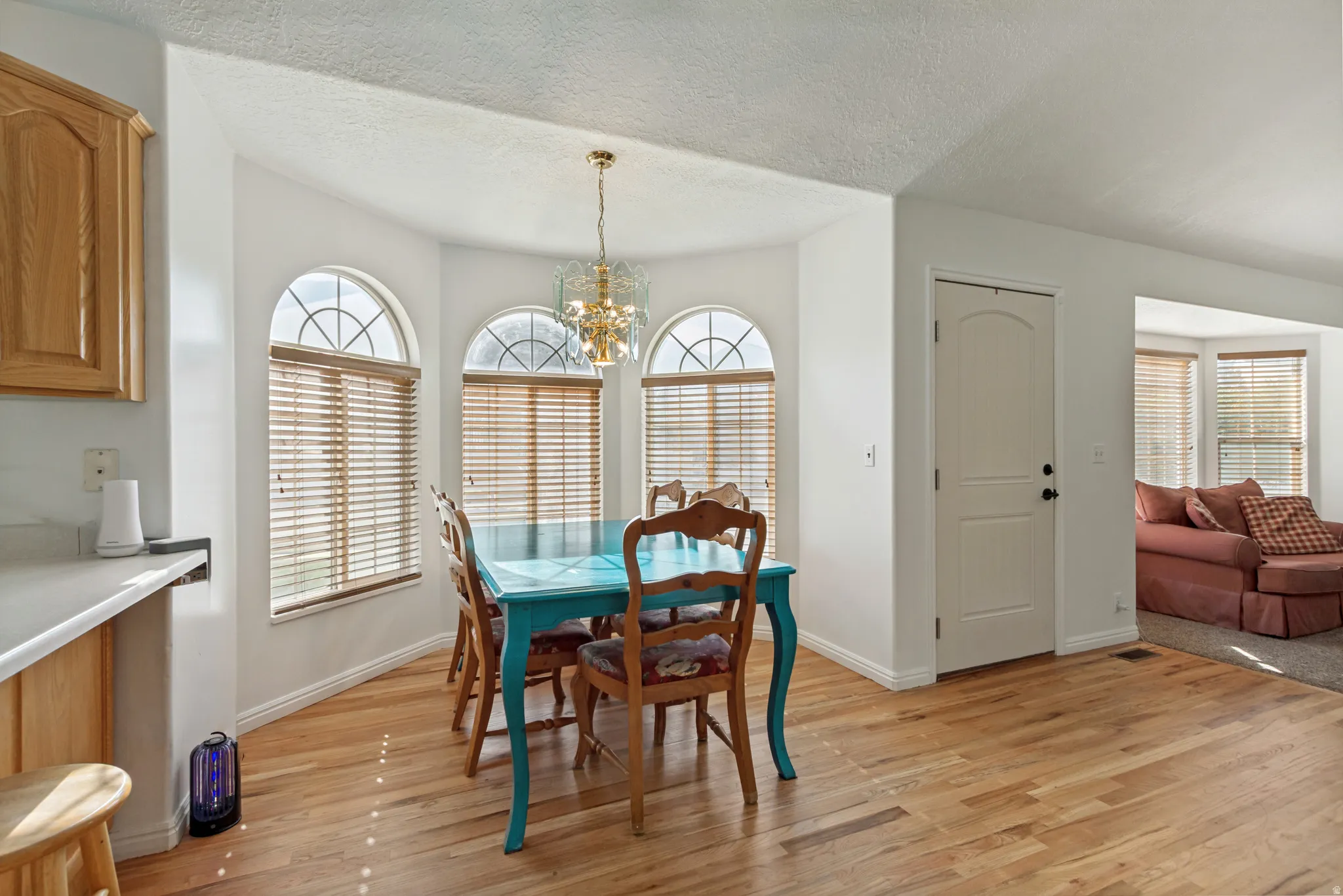 Dining area featuring light wood-finish flooring, a decorative chandelier, and a bay window with three arched windows