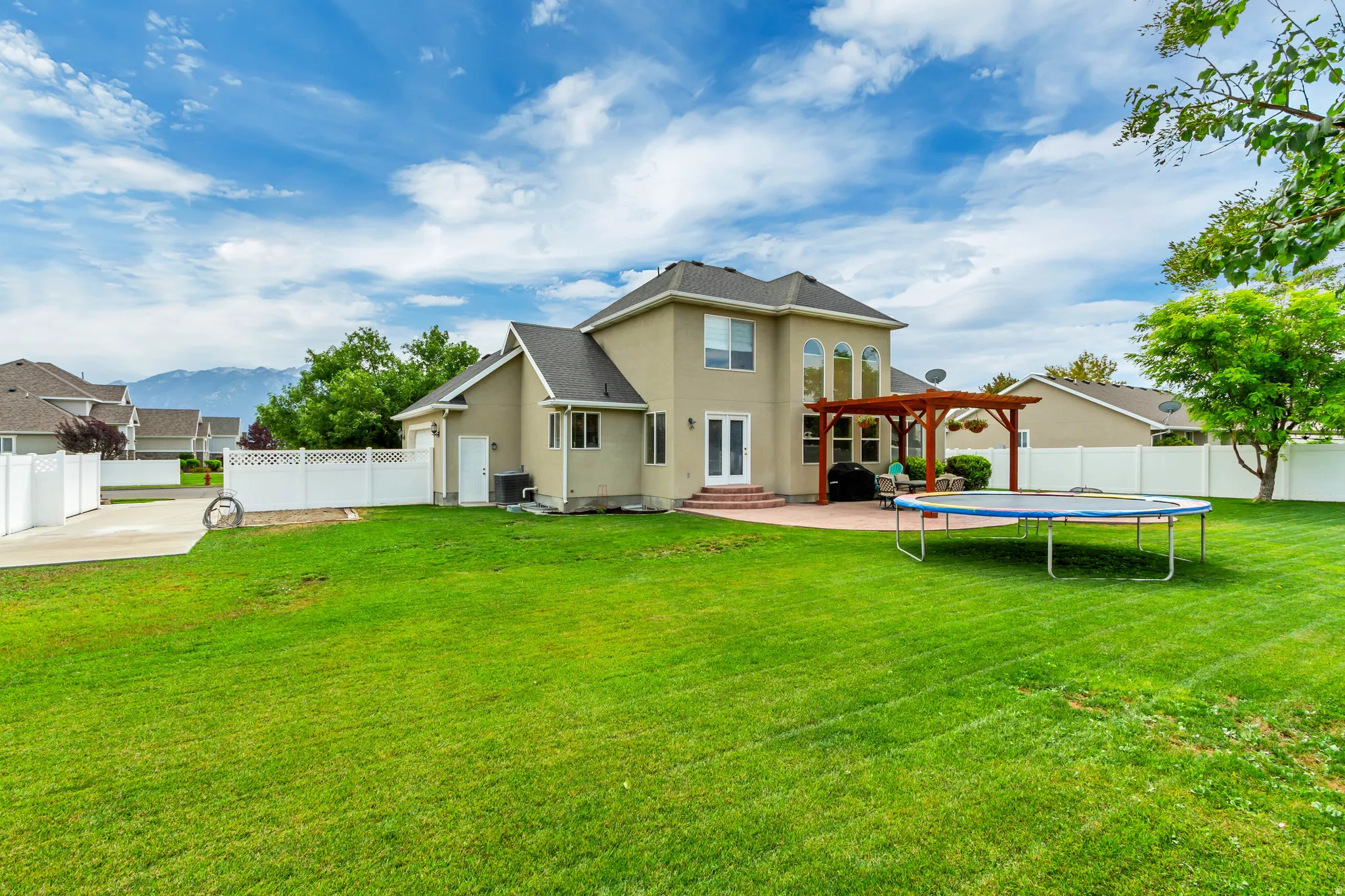 Expansive rear lawn featuring a large patio, built-in pergola, and double French doors