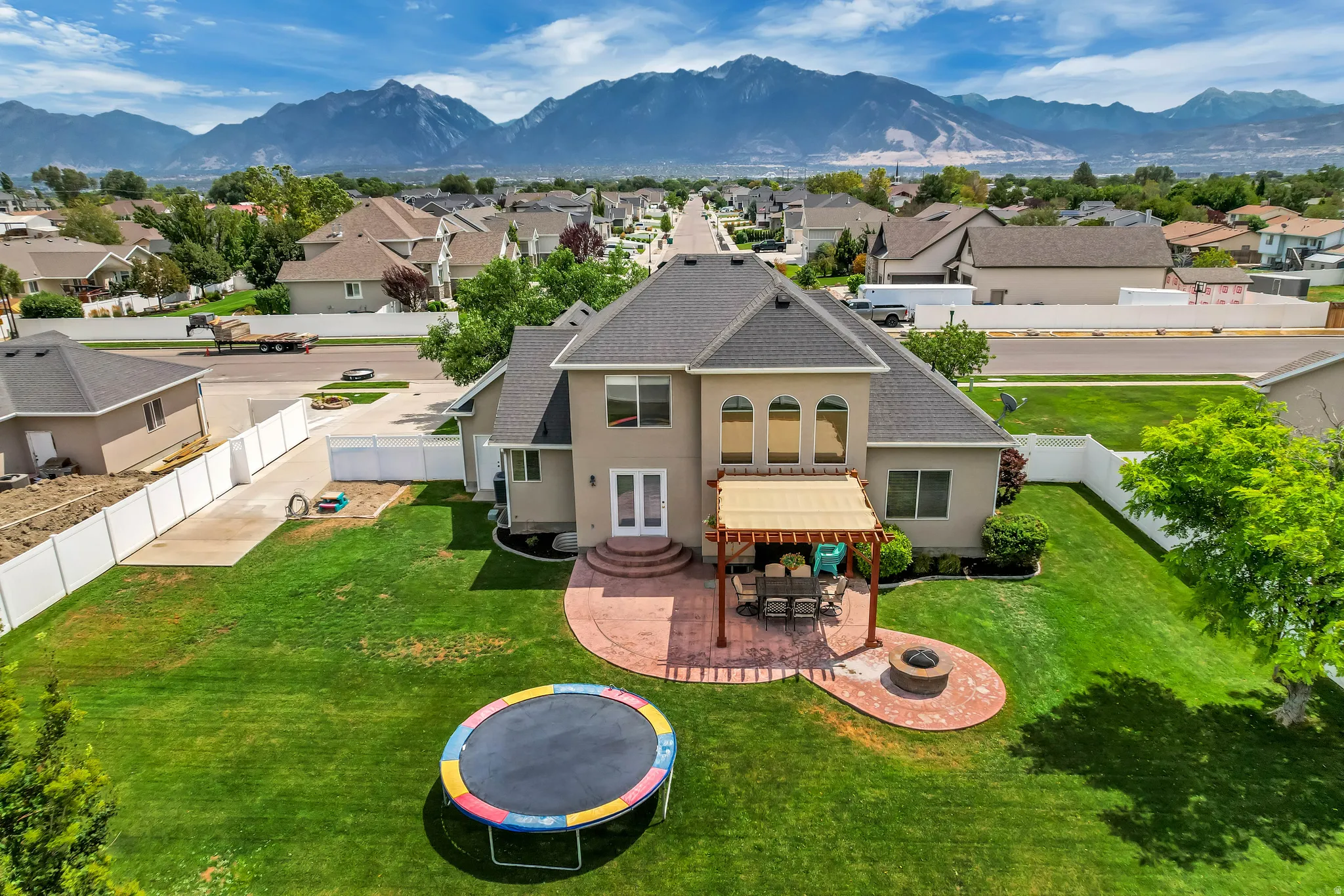 Spacious backyard featuring a large green lawn, a brick paver patio with a pergola, a built-in fire pit, and a double-door exterior entry