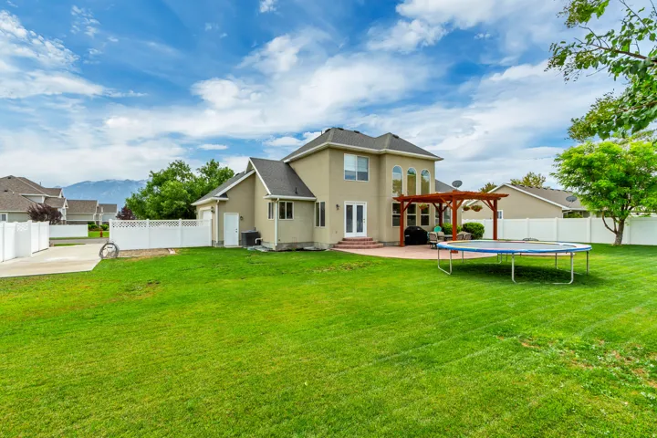Expansive rear lawn featuring a large patio, built-in pergola, and double French doors