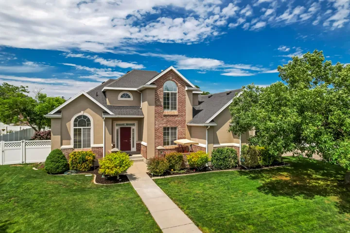 Stucco and brick exterior with arched window accents, a dark red entry door, a manicured lawn, and mature landscaping