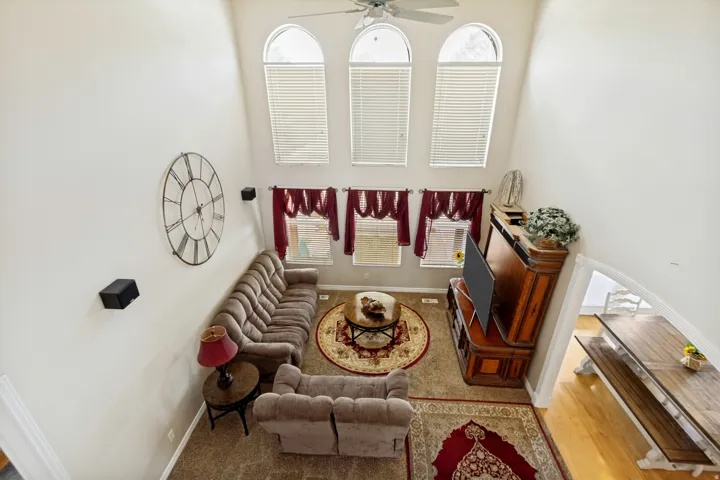 Living area featuring vaulted ceilings, three arched windows with blinds, and a ceiling fan