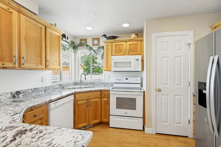 Kitchen featuring wood cabinetry, light-toned countertops, built-in microwave, white electric range, and wood-finish flooring