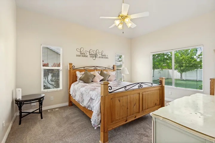 Spacious bedroom featuring vaulted ceilings, a ceiling fan with light fixture, broad window with horizontal blinds, and a secondary vertical window