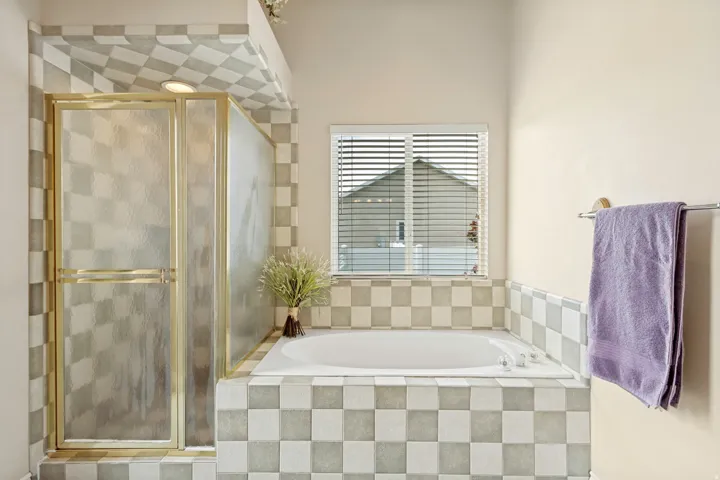 Bathroom featuring a spacious built-in tub with checkerboard tile surround and a separate shower enclosure with a gold-toned frame and frosted glass panels