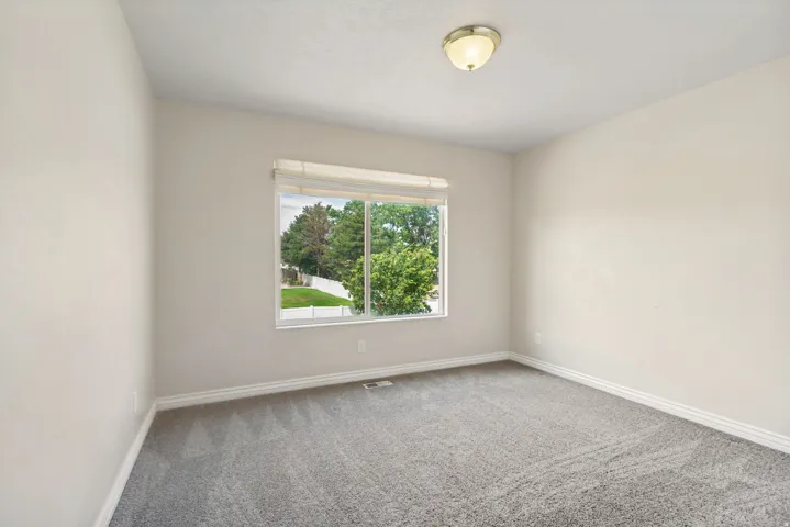 Room featuring a window with exterior views of trees, light gray carpet, white baseboards, and neutral-toned walls