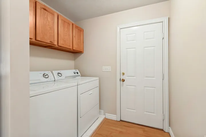 Laundry area featuring light wood-finish flooring, white paneled door, and built-in wood cabinetry