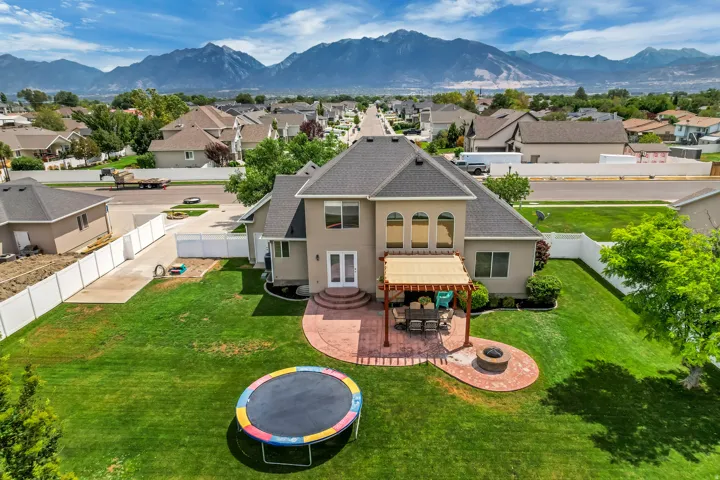 Spacious backyard featuring a large green lawn, a brick paver patio with a pergola, a built-in fire pit, and a double-door exterior entry