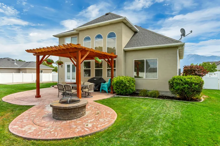 Expansive backyard featuring a stained wood pergola over a stamped concrete patio with a built-in stone fire pit