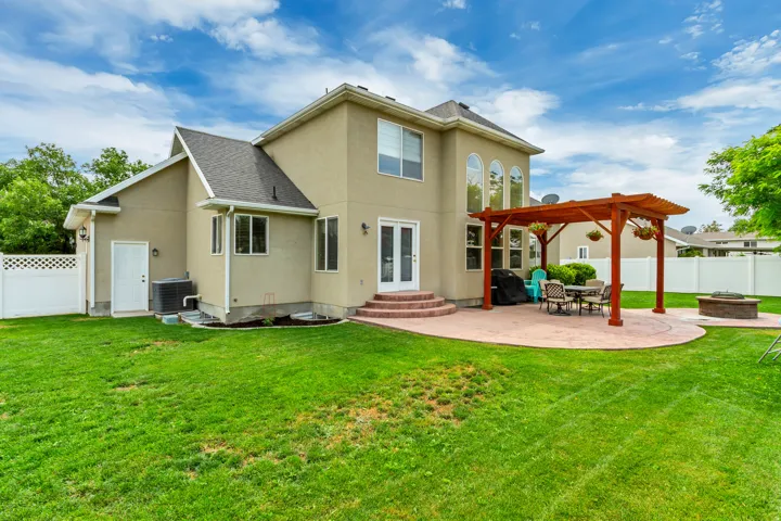 Rear exterior featuring a spacious lawn, a stamped concrete patio, and a wood pergola