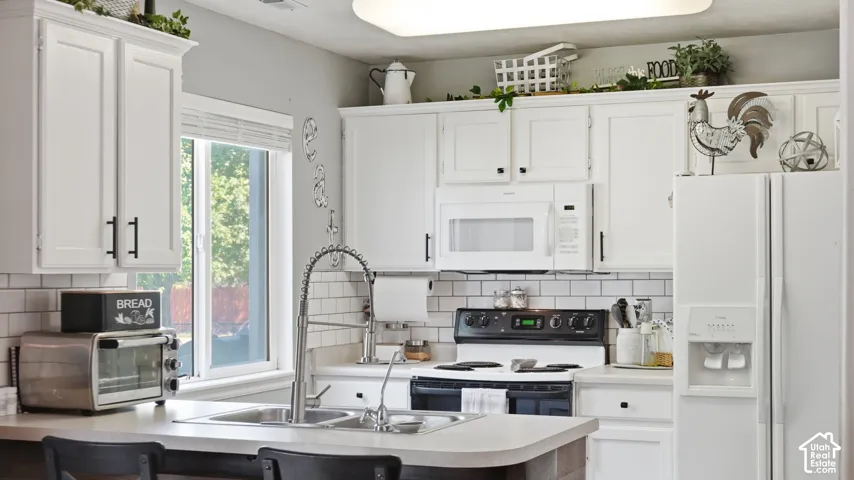 Kitchen featuring white cabinetry, subway tile backsplash, stainless steel sink with a gooseneck faucet, white appliances, and a window