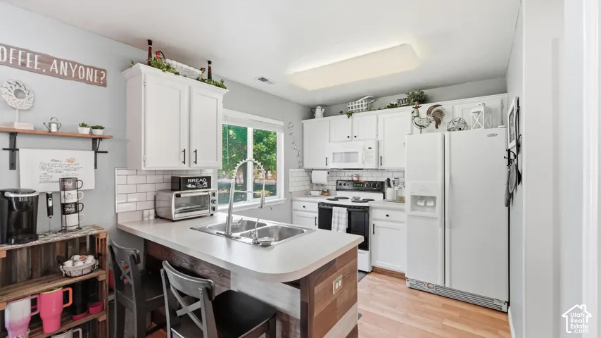 Kitchen featuring white cabinetry, subway tile backsplash, light countertops, wood-finish flooring, and a stainless steel double basin sink with a gooseneck faucet