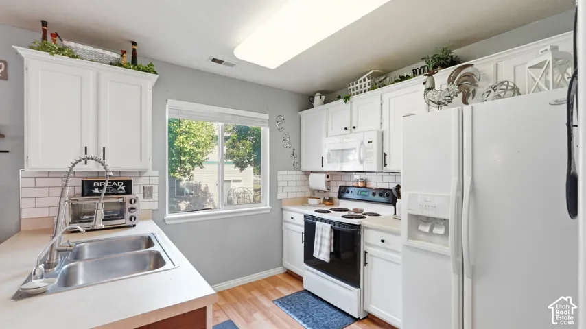 Kitchen featuring white cabinetry, light countertops, subway tile backsplash, stainless steel double basin sink with a high-arc faucet, and hardwood-finish flooring