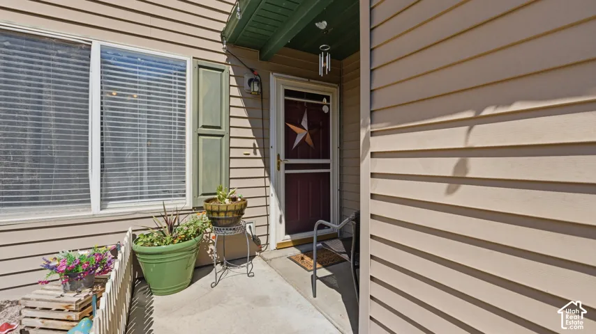 Entryway featuring beige horizontal siding, a red front door with a storm door, and a covered porch